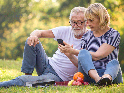 Happy senior couple relaxing in park using smartphone together . old people sitting on grass in the summer park looking mobile phone . Elderly resting .mature relationships