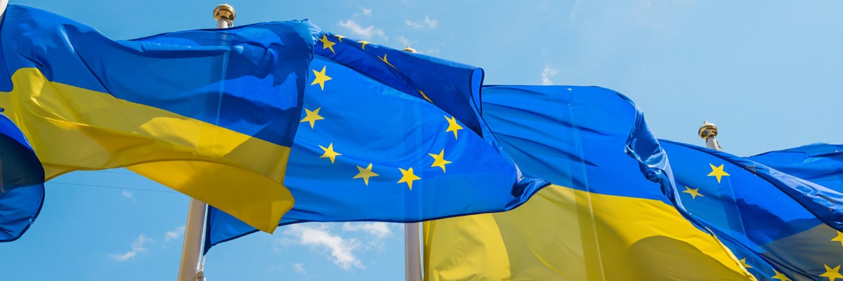Row of flag poles with European Union and Ukraine flags fluttering by wind on blue sky background